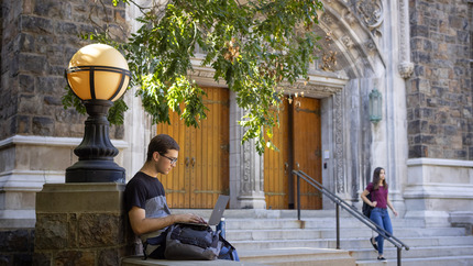 Student sitting outside a building on his computer.